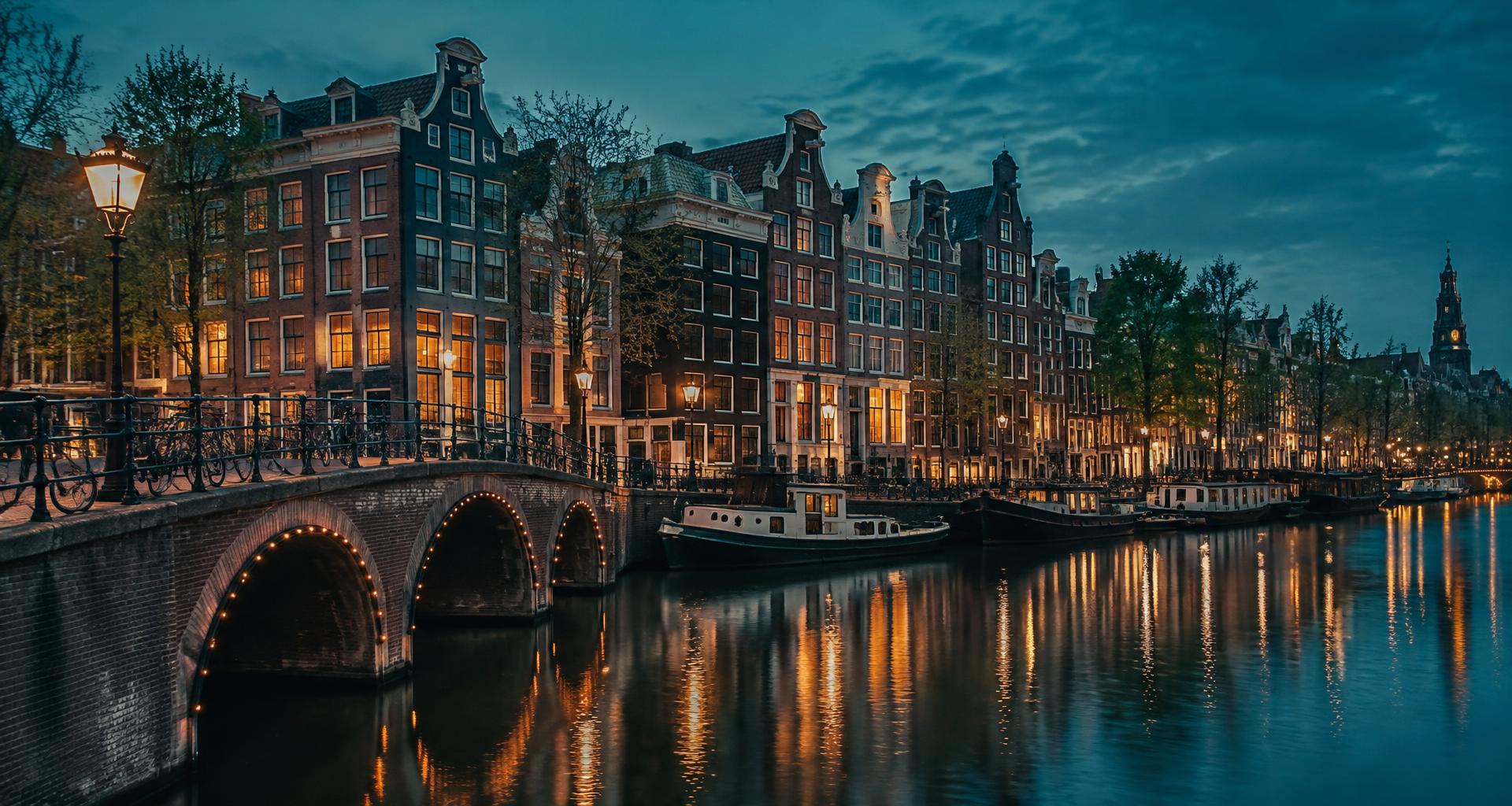 Amsterdamse grachtenpanden en een verlichte brug aan de gracht bij avond